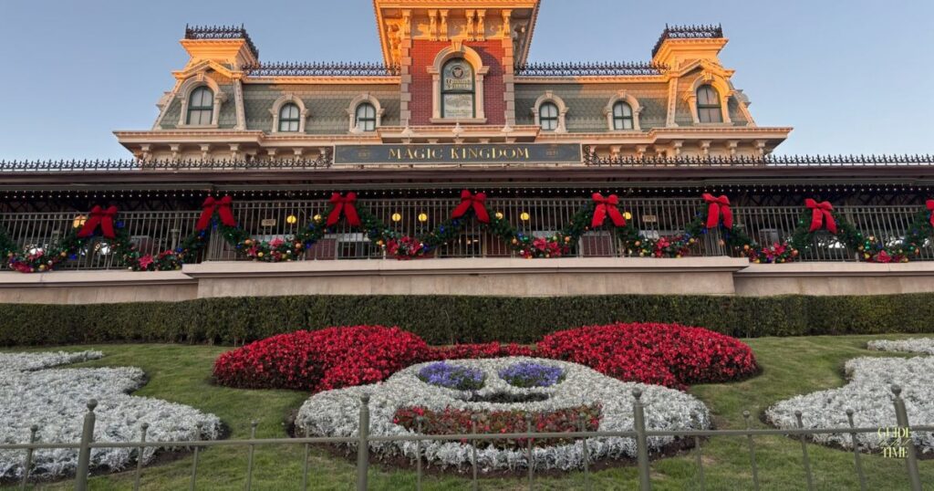Magic Kingdom's Main Street train station with red bows and garland above the Mickey flower bed at dusk